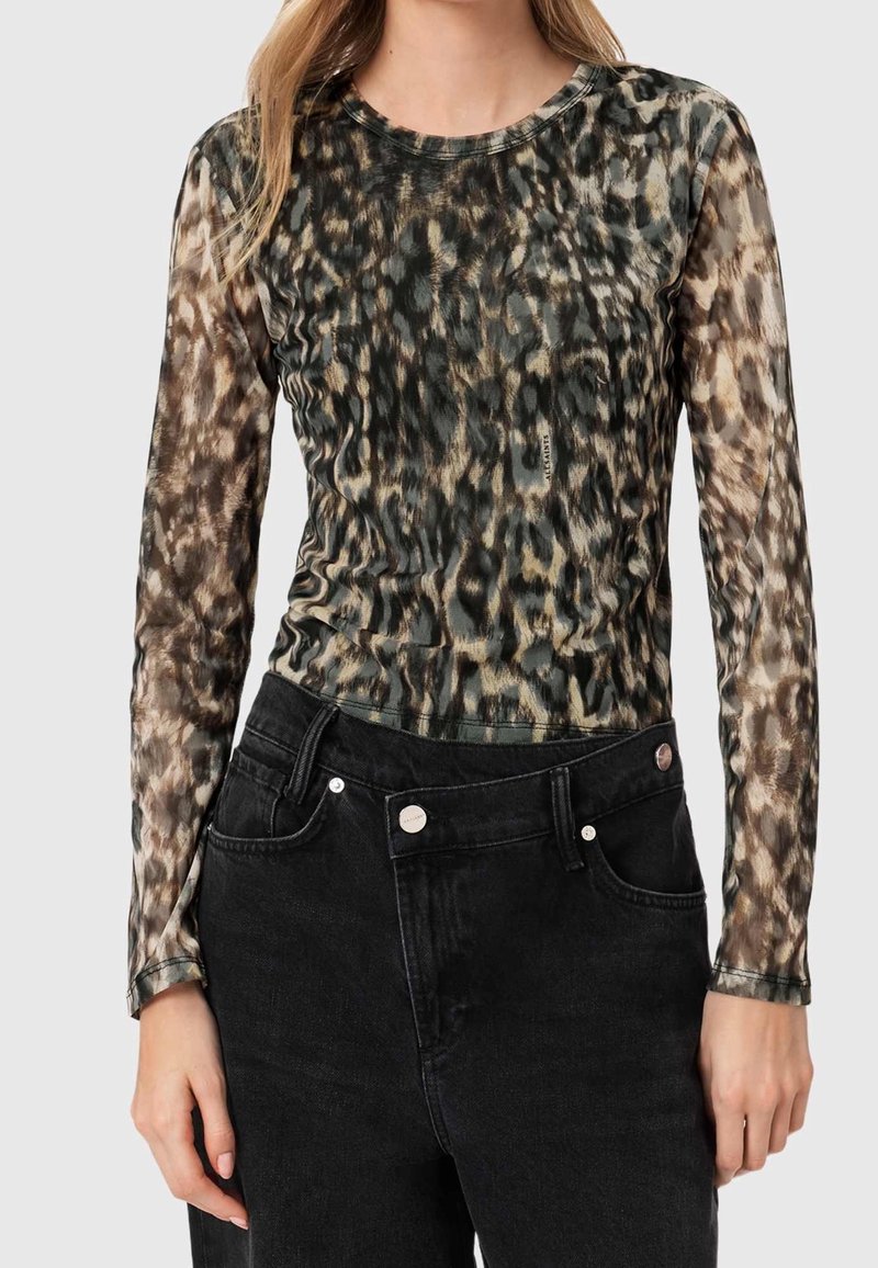 Femme portant un haut transparent à manches longues avec un imprimé animalier et un jean noir taille haute avec un bouton et des poches avant.
