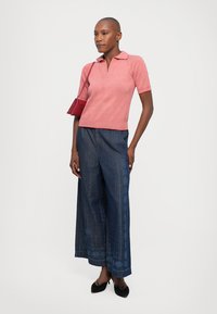 Polo a righe rosse e bianche con maniche corte, abbinato a pantaloni denim blu a gamba larga con un motivo testurizzato sul lato.