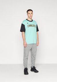 Una camisa de manga corta en verde menta y negro con "CHARLOTTE" en letras doradas, combinada con pantalones deportivos grises y zapatillas negras.