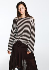 Brown and white striped long-sleeve top with a relaxed fit, paired with a dark flowing skirt that features sheer accents.