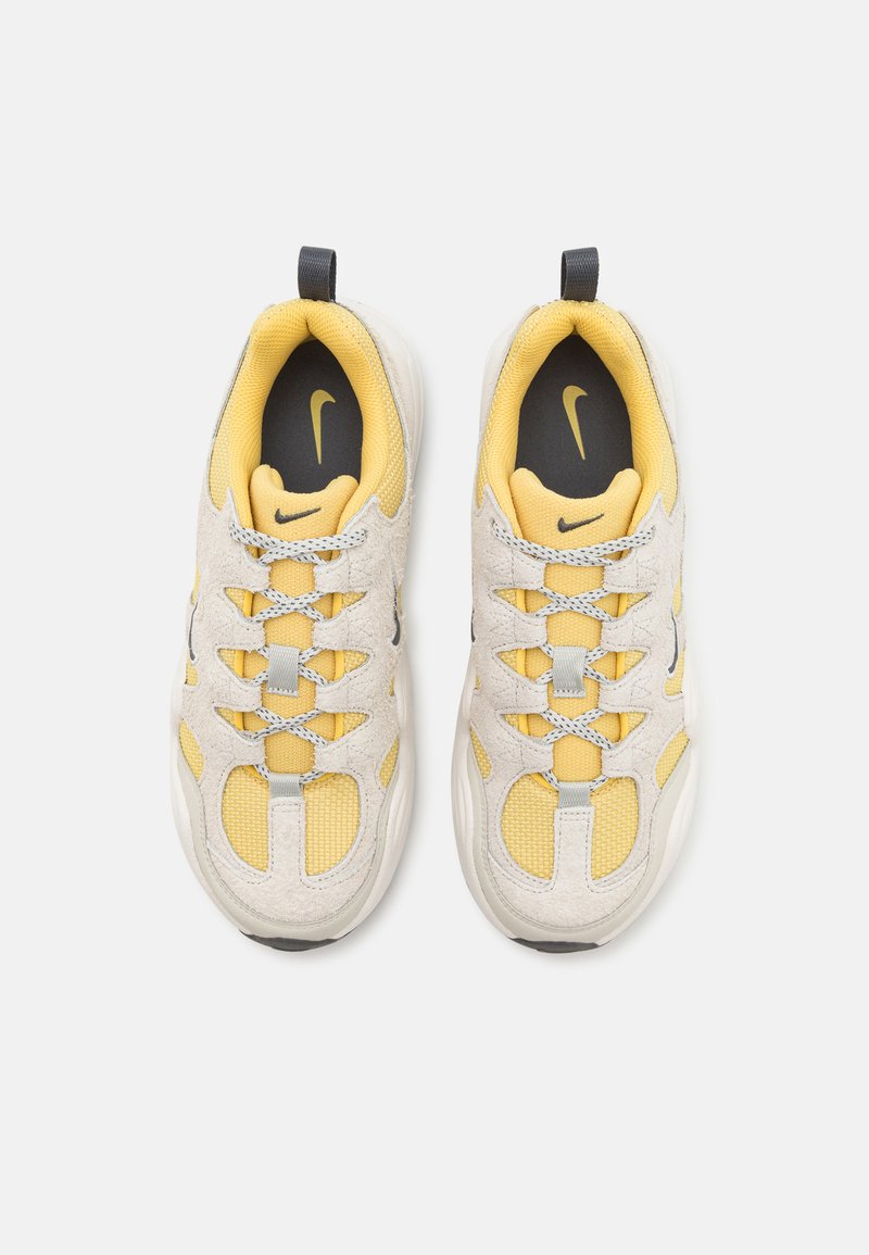 Baskets sportives avec un design en suède et mesh beige et jaune, un système de laçage gris et un logo noir sur la semelle intérieure.