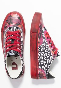 Baskets rouges et noires avec un motif léopard, dotées d'un tissu texturé, de lacets plats et d'une semelle en caoutchouc avec des accents subtils en rose.