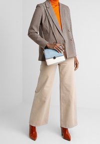 Hnědý kostkovaný blazer, oranžový rolák, béžové kalhoty s širokými nohavicemi, lesklé červené kotníkové boty a dvoubarevná kabelka s řetízkovým držadlem.