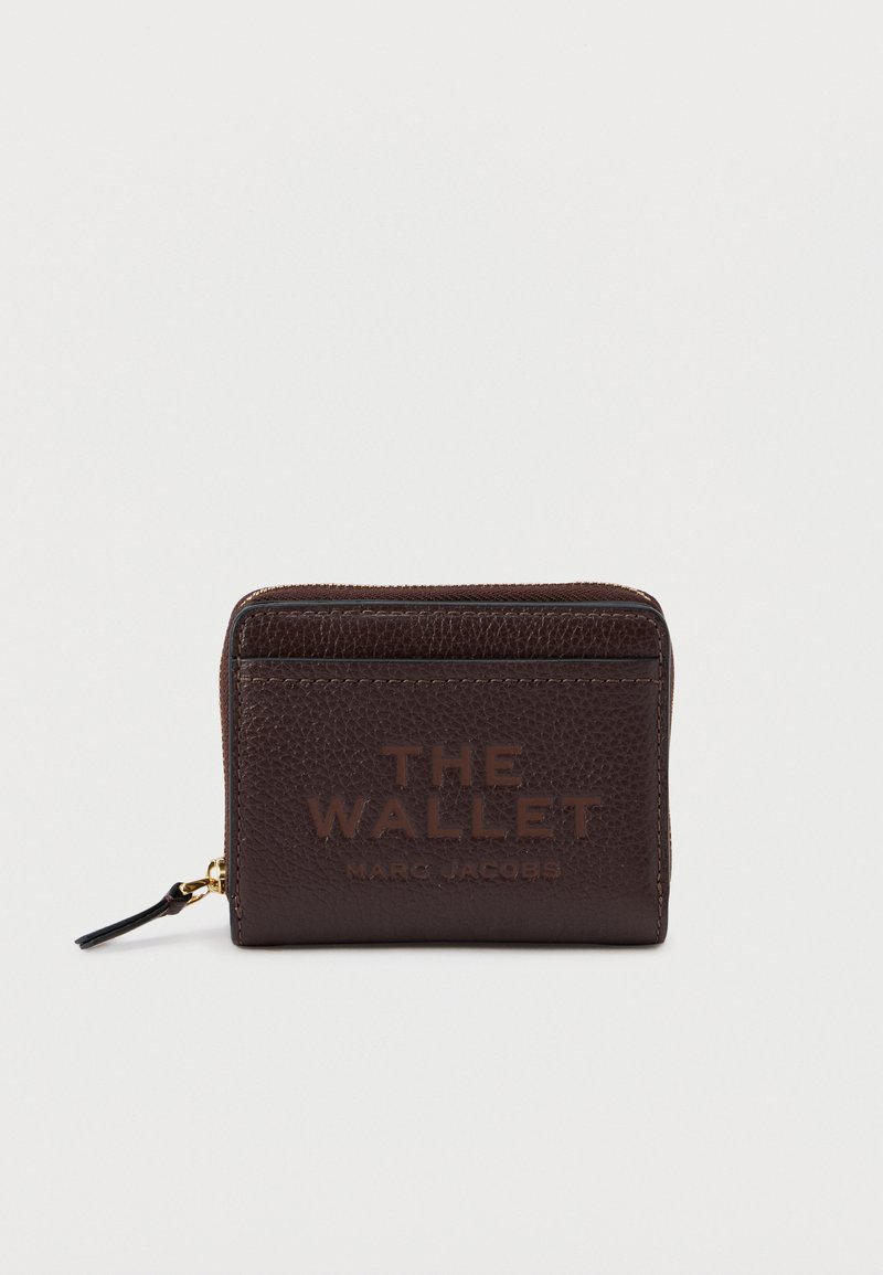 Portafoglio in pelle marrone con finitura testurizzata. Presenta la scritta in rilievo "THE WALLET" e "MARC JACOBS" sulla parte anteriore e una chiusura con zip.