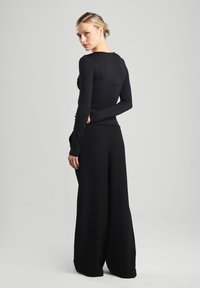 Black long-sleeve top with a round neckline, paired with wide-leg black pants. Smooth fabric with a fitted silhouette and minimal design.