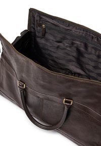 Sac fourre-tout en cuir brun foncé avec une fermeture éclair dorée, des poignées arrondies et une poche intérieure en tissu noir à motifs avec fermeture éclair.