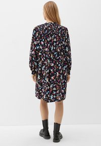Blumenmusterkleid mit dunklem Hintergrund, langen puffärmel, elastischem Smocking am Ausschnitt und knielangem Saum. Getragen mit schwarzen Knöchelstiefeln.