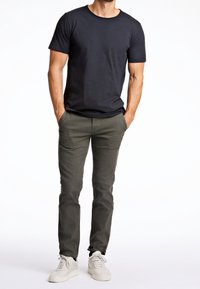 Svart bomulls-t-shirt med rund halsringning, kombinerad med olivgröna chinos och vita sneakers. Enkel design, figurnära silhuett.