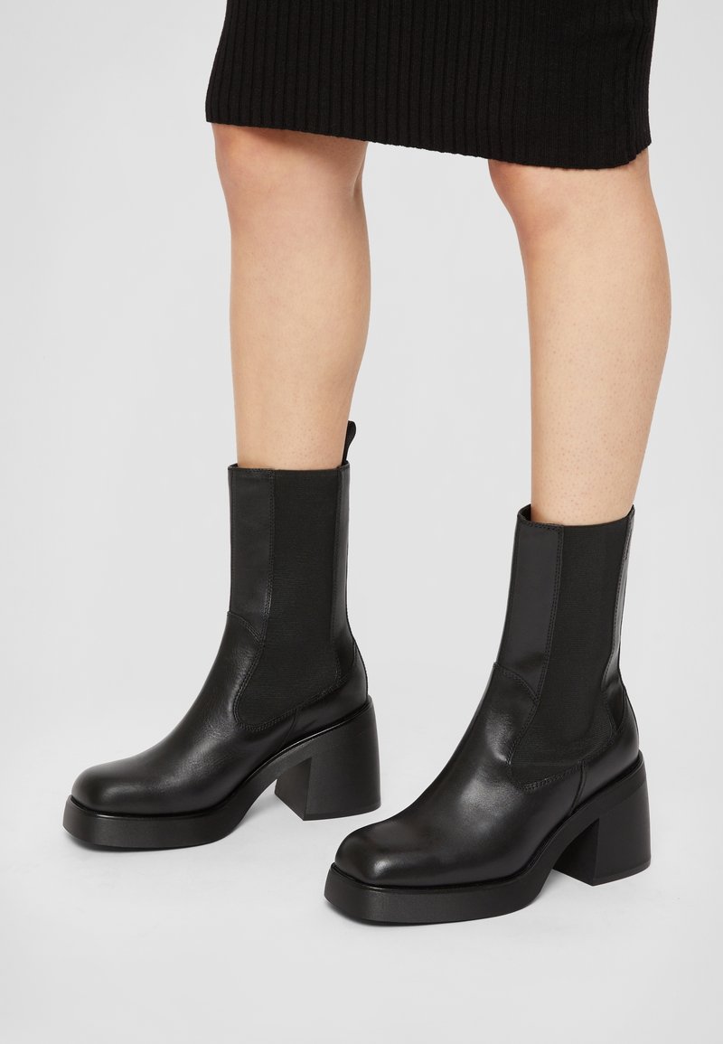 Czarne botki za kostkę wykonane z gładkiej skóry, wyposażone w elastyczne boczne panele oraz grube, masywne obcasy o matowym wykończeniu.