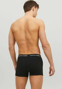 Shirtless man facing away wearing black Jack & Jones boxer briefs with branded waistband against plain light gray background.