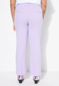 Lichtpaarse broek met rechte pijpen en twee achterzakken. De stof lijkt glad, aangevuld met metallic roze hakken.