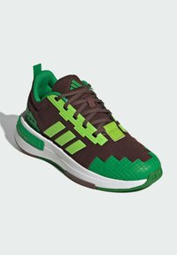 Hnedá a zelená športová obuv s textúrovaným zvrškom, veľkými zelenými akcentmi a bielou podrážkou. Obsahuje pixelované detaily a pútko na päte.
