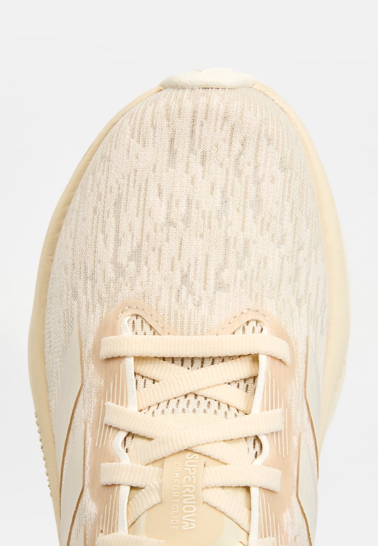 Zapatilla deportiva beige con parte superior de tejido texturizado, rayas tonalidades y cordones planos. Cuenta con suela acolchada y detalles de logo.