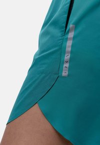 Teal atletikshorts lavet af letvægtsstof, med et struktureret mønster og et sølvlogo på sidesømmen.