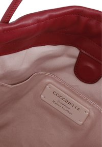Interno di una borsa in pelle rossa con foderatura in tessuto rosa chiaro, con un'etichetta che recita "Coccinelle Pelle Italiana Autentica".