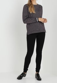 Suéter de punto multicolor con mangas largas y puños a rayas, combinado con leggings negros ajustados y zapatos negros brillantes.