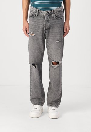 Grey distressed denim jeans with large rips at knees, straight-leg cut, and a faded finish. Paired with white sneakers.
