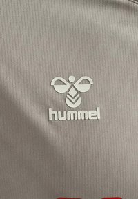 Grau athletisches Gewebe mit einer vertikalen gerippten Struktur; zeigt ein weißes Logo einer Biene und darunter in fetten Buchstaben das Wort "hummel".
