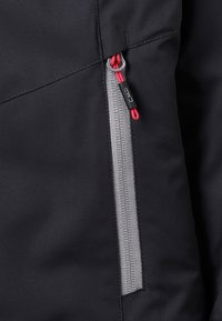 Czarna kurtka z szarym kieszonkowym zamkiem błyskawicznym i czerwonym uchwytem. Gładka struktura materiału z aerodynamicznym kształtem i minimalistycznymi akcentami.