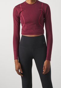 Top corto a maniche lunghe bordeaux con cuciture di accento rosa, abbinato a leggings neri a vita alta. Tessuto morbido, scollatura rotonda.