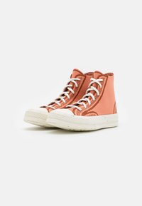 Sapatilhas altas em tecido coral suave com atacadores brancos, detalhes texturizados, e uma sola de borracha creme com um padrão texturizado à volta da ponta.
