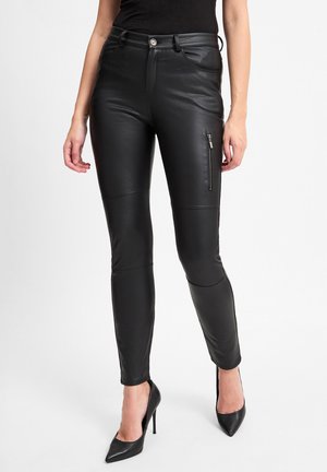 Black faux leather skinny pants with a zippered pocket on the side, fitted design, smooth texture, and accent stitching, paired with black heels.