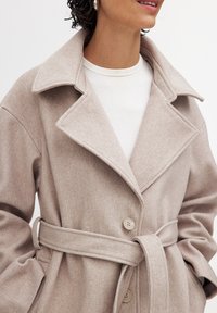 Helebeež villasegu mantel suure kraega, topelt nööbiga kinnitamine ja vöö. Pehme tekstuur, kohandatud lõige ja ülekaalulised varrukad.