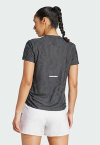 Maglietta atletica grigia a maniche corte con un motivo geometrico, tessuto leggero e dettaglio riflettente sulla schiena, abbinata a pantaloni corti bianchi.