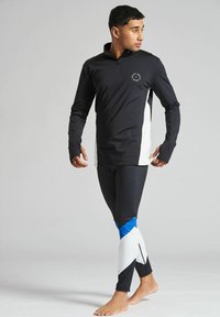 Svart långärmad atletisk topp med vit sidopanel och logotyp, tillsammans med figurnära svarta leggings med blå och vit geometrisk mönstring.