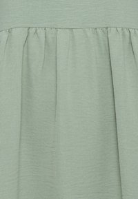 Ljust grönt, texturerat tyg med en samlad midjedetalj, som visar en mjuk hängning och subtil glans, lämpligt för olika klädesapplikationer.