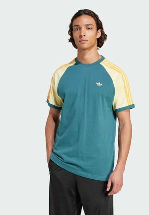 Teal cotton t-shirt with yellow raglan sleeves, ribbed crew neck, and three yellow stripes on each shoulder. Small gold logo on chest.