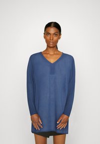 Tunica blu a maniche lunghe con scollo a V e motivo testurizzato, realizzata in tessuto leggero, caratterizzata da una vestibilità ampia e spacchi laterali.