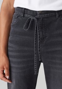 Pantalones de mezclilla gris carbón con cintura atada, diseño de cinco bolsillos y detalles de costura visibles. La tela tiene un acabado ligeramente texturizado.