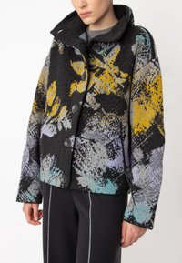 Blůza na knoflíky s černým základem a živými květinovými vzory v žluté, fialové a tyrkysové barvě, vyrobená z texturované látky.