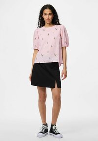 Blusa rosa con texture e motivi floreali, abbinata a una mini gonna nera con uno spacco laterale. Scarpe da ginnastica alte nere completano l'outfit.