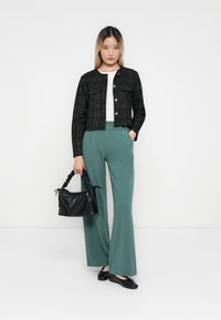 Svart tweed cropped jakke med sølvknapper, parret med høyt liv grønne vidde bukser. Holder en liten svart håndveske.