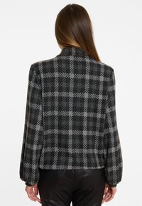 Karierte Jacke in Schwarz und Grau, mit einem strukturierten Kragen und gepufften langen Ärmeln, aus einem weichen Stoff mit taillierter Passform.