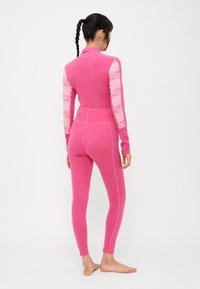 Conjunto térmico rosa ajustado com mangas longas, gola alta e realces de padrão texturizado nas mangas, tecido canelado e leggings até ao tornozelo.