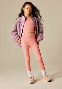 Top corto rosa a coste e leggings coordinati a vita alta, abbinati a una giacca lavanda pelosa. Sneakers rosa con dettagli bianchi e rosa.