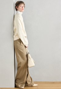 Suéter beige de punto, cuello alto crema, pantalones anchos marrones y un pequeño bolso beige. Diseño sencillo con colores neutros y texturas suaves.