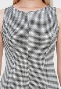 Svart och vit houndstooth-mönstrad ärmlös klänning med rundad halsringning och figurnära silhuett. Texturerad vävd tyg.