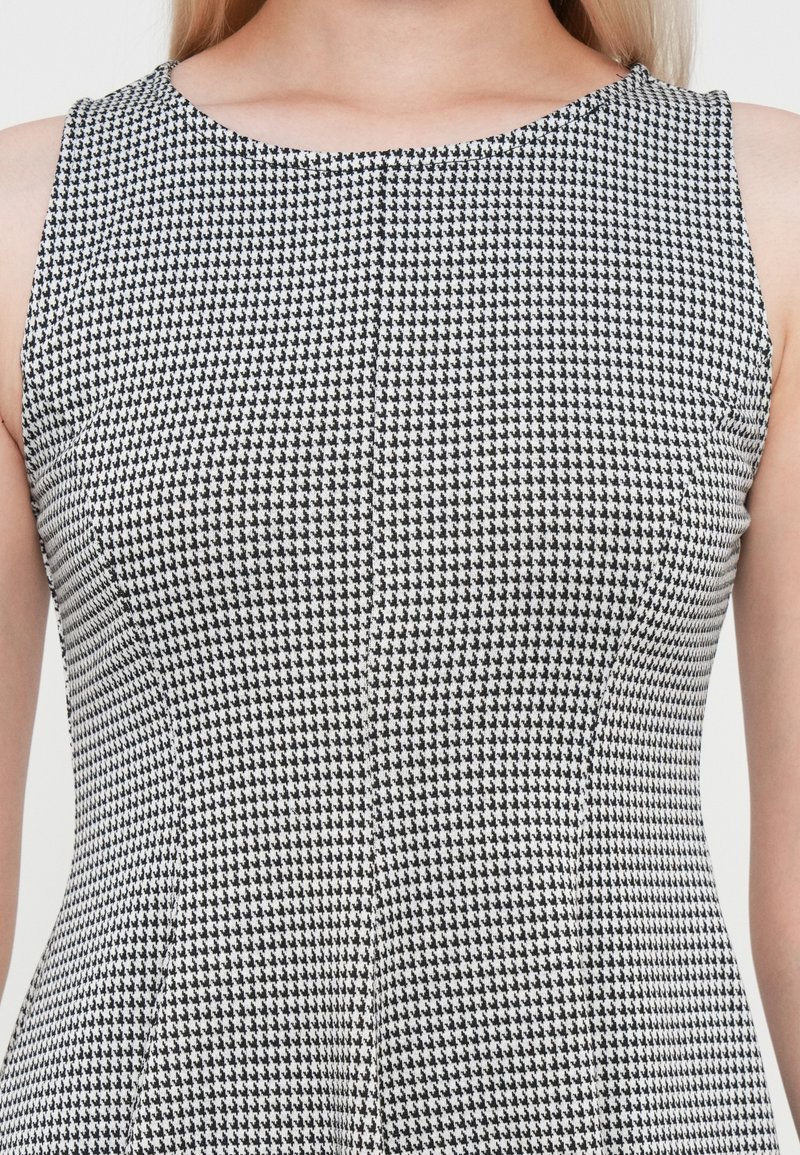 Robe sans manches à motif pied-de-poule noir et blanc, avec un décolleté arrondi et une silhouette ajustée. Tissu tissé texturé.