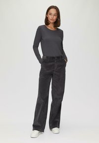 Grijze top met lange mouwen gecombineerd met hoge taille, wijde zwarte corduroy broek. Model draagt witte sneakers. Effen achtergrond.