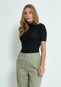 Bodysuit negro de manga corta con cuello alto, combinado con pantalones verdes claros de cintura elástica. Textura suave, diseño ajustado.