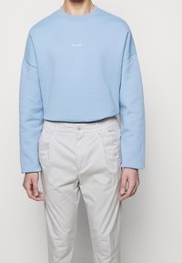 Felpa azzurro chiaro con spalle scese e scollo tondo, con delicato testo del logo bianco. Abbinata a pantaloni beige chiaro con vita elastica.