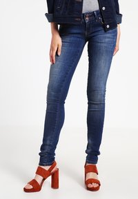 Mörkblå denim skinny jeans med en klassisk femficksdesign, kombinerat med bruna mocka högklackade sandaler med blockklack.