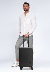 Schwarzer Hartschalenkoffer mit zwei ausziehbaren Griffen und vier Rädern. Strukturiertes Finish, minimalistisches Design. Geeignet für Reisen.