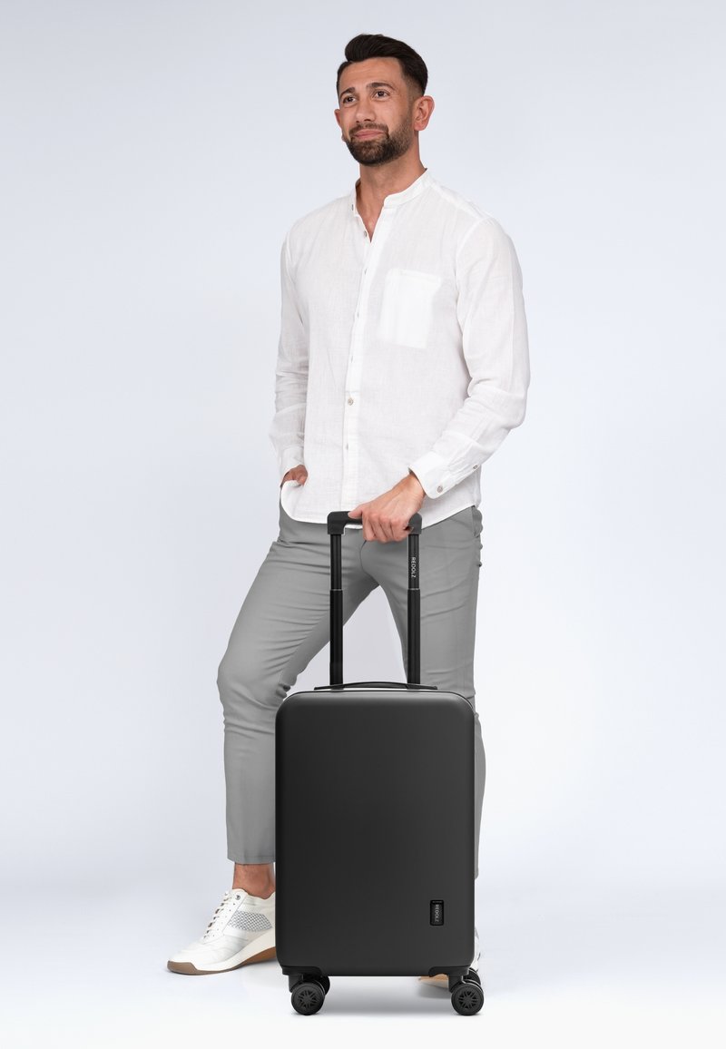 Schwarzer Hartschalenkoffer mit zwei ausziehbaren Griffen und vier Rädern. Strukturiertes Finish, minimalistisches Design. Geeignet für Reisen.