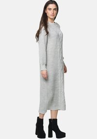 Abito midi grigio a maglia con un motivo a treccia testurizzato, maniche lunghe e polsini a coste. Abbinato a stivaletti neri alla caviglia.