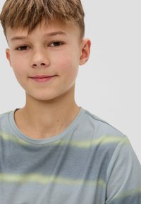Šviesiai mėlyna marškinė su horizontaliomis žaliomis ir tamsiai mėlynomis juostelėmis. Trumpi rankovės ir apvalus iškirpimas, pagaminta iš minkštos medžiagos.